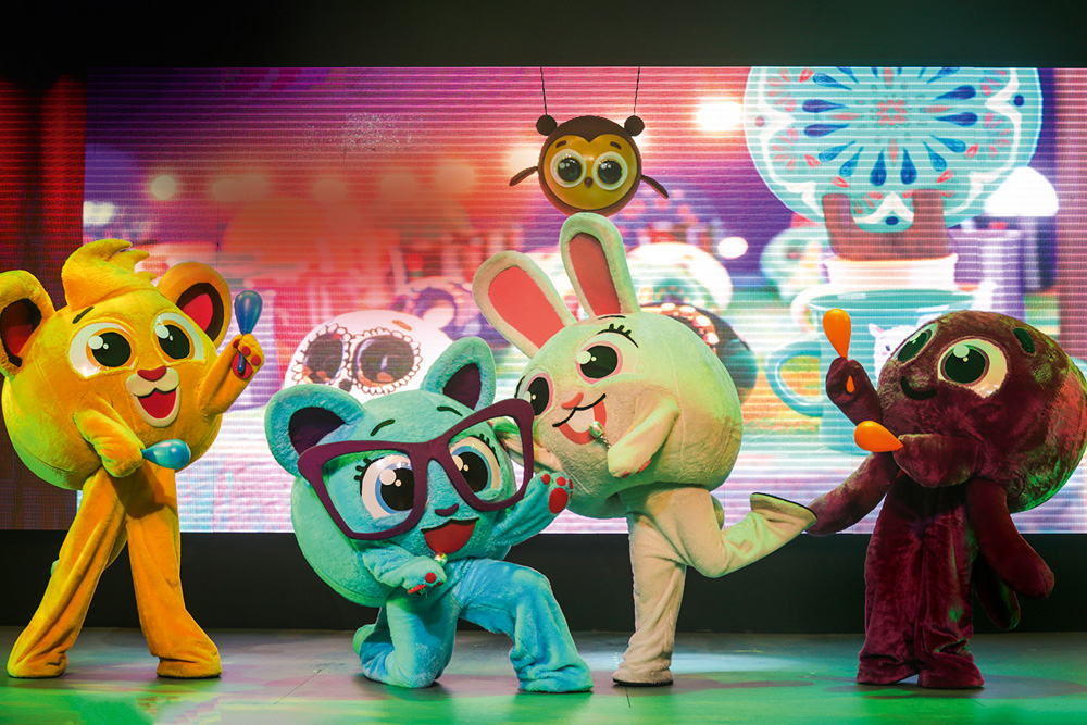 10 – Fadelito (Helena Mello-Divulgação) Grandes bonecos em um palco posam dançando. Todos têm figuras animalescas, como coelhos, e ao fundo aparece um telão iluminado.