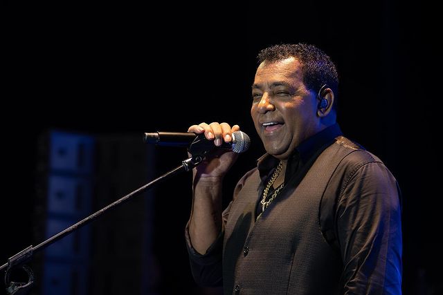 a imagem mostra o cantor luiz carlos, um homem negro com roupa social e o microfone na mão em cima de um palco