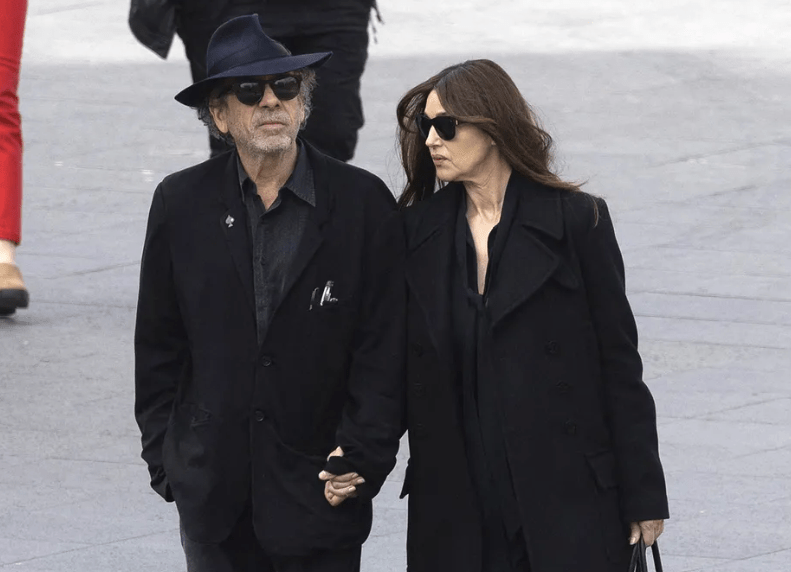 Tim Burton e Monica Belluci de roupas escuras andando de mãos dadas na rua