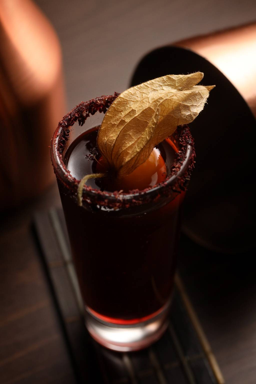 Carrasco Drink roxo em copo alto com borda com crosta roxa e fisális por cima.