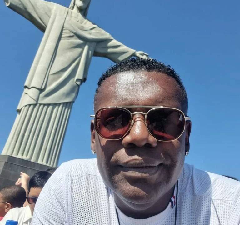 o cantor MC marcinho olha para a câmera de óculos escuros e atrás dele está o cristo redentor