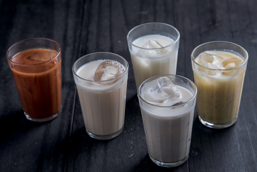 Batidas de cores e sabores variados no copo americano em fundo cinza.