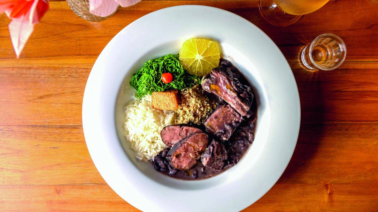 Foto aérea de prato de feijoada sobre mesa de madeira.