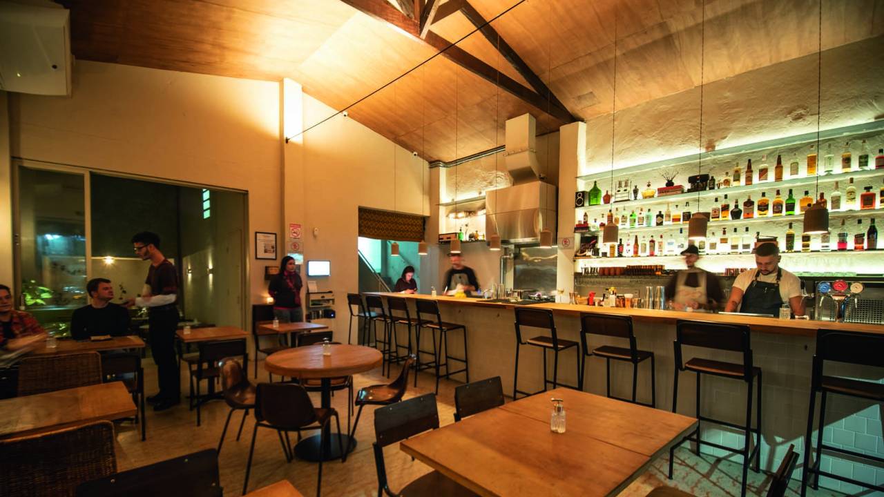 Salão do bar Jabali, com mesinhas de madeira e balcão com banquetas ao fundo à direita.