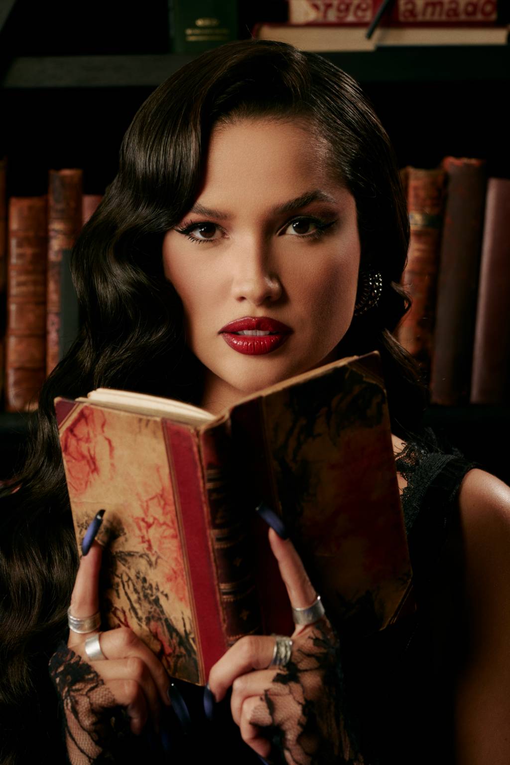 Juliette (Juliana Rocha-Divulgação) Mulher branca segura livro antigo com dedos indicadores em destaque. Tem cabelos pretos levemente encaracolados e batom bem vermelho.