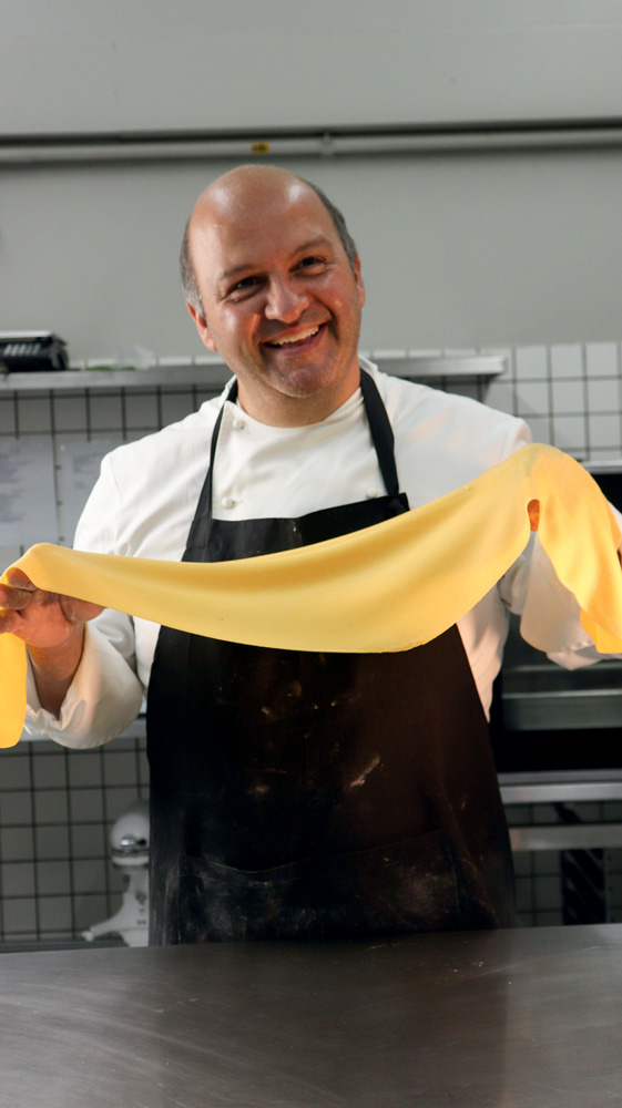 Homem de avental sorrindo para foto enquanto estica massa.