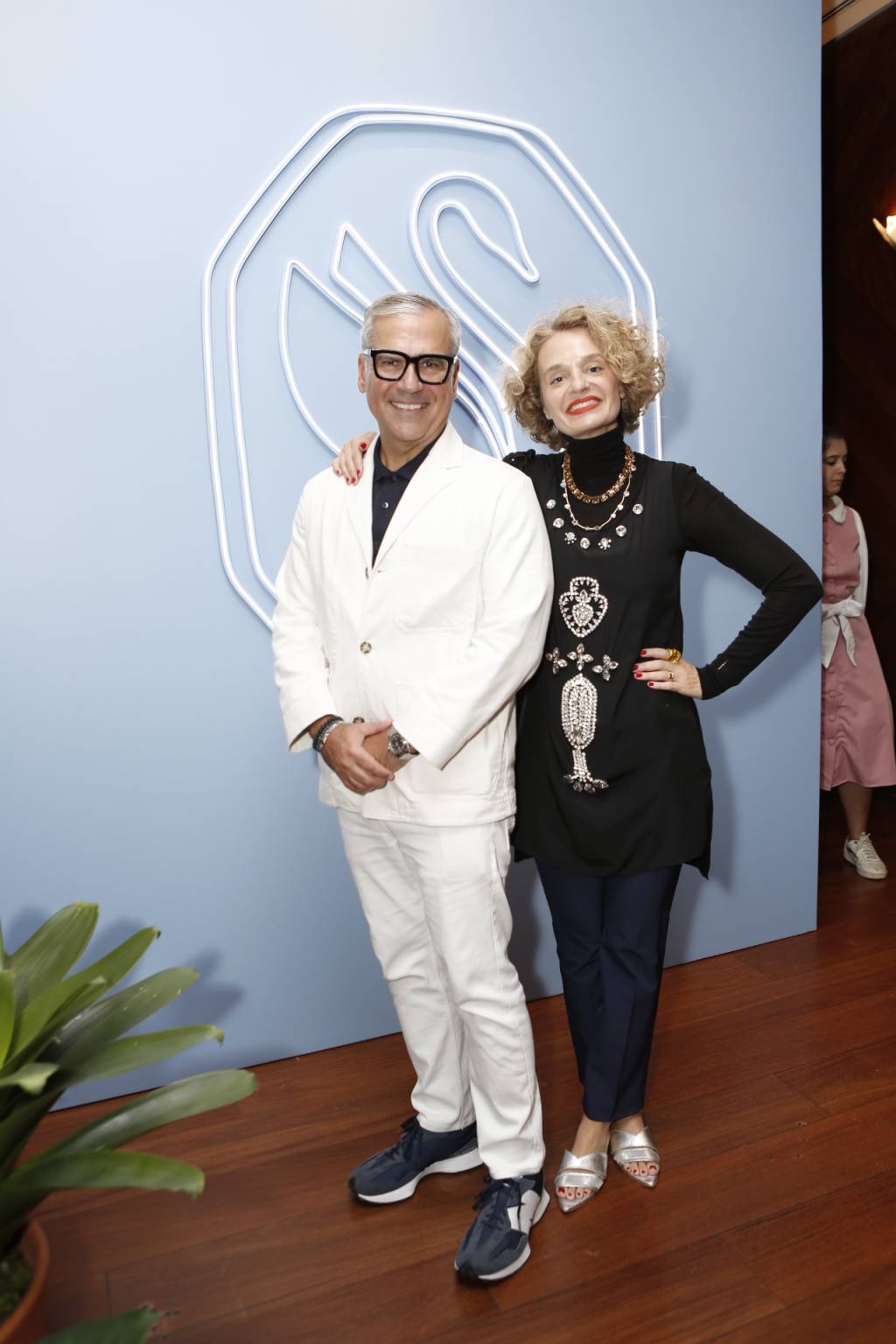 Brunch Swarovski (Kenji Nakamura) Homem e mulher posam de pé lado a lado. Ele veste terno branco e óculos de grau pretos. Ela veste roupa toda preta e joias.