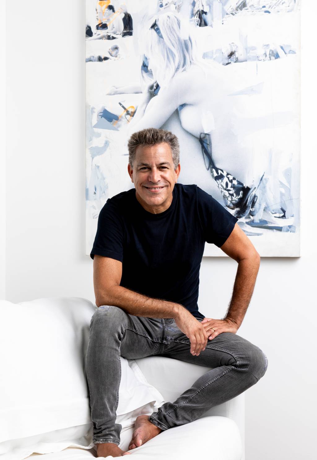 Luiz Calainho (Sérgio Zalis-Divulgação) Homem grisalho posa em cima de sofá branco, descalço, com calça jeans e camiseta preta.