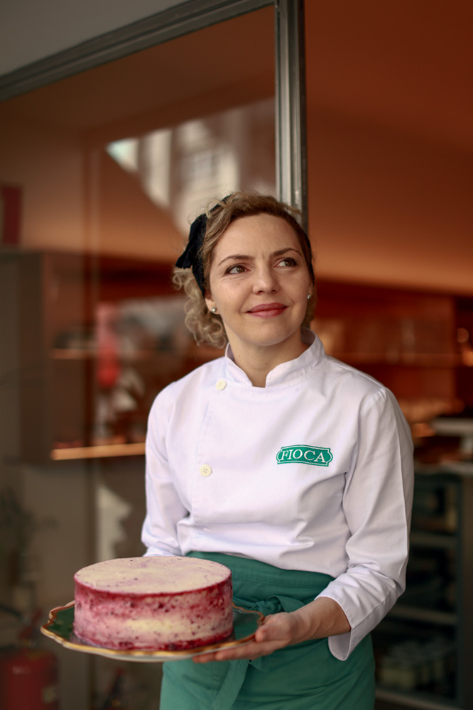 Doces saudáveis – Fioca – Regina Paula Mulher de dólmã e avental segurando bolo.