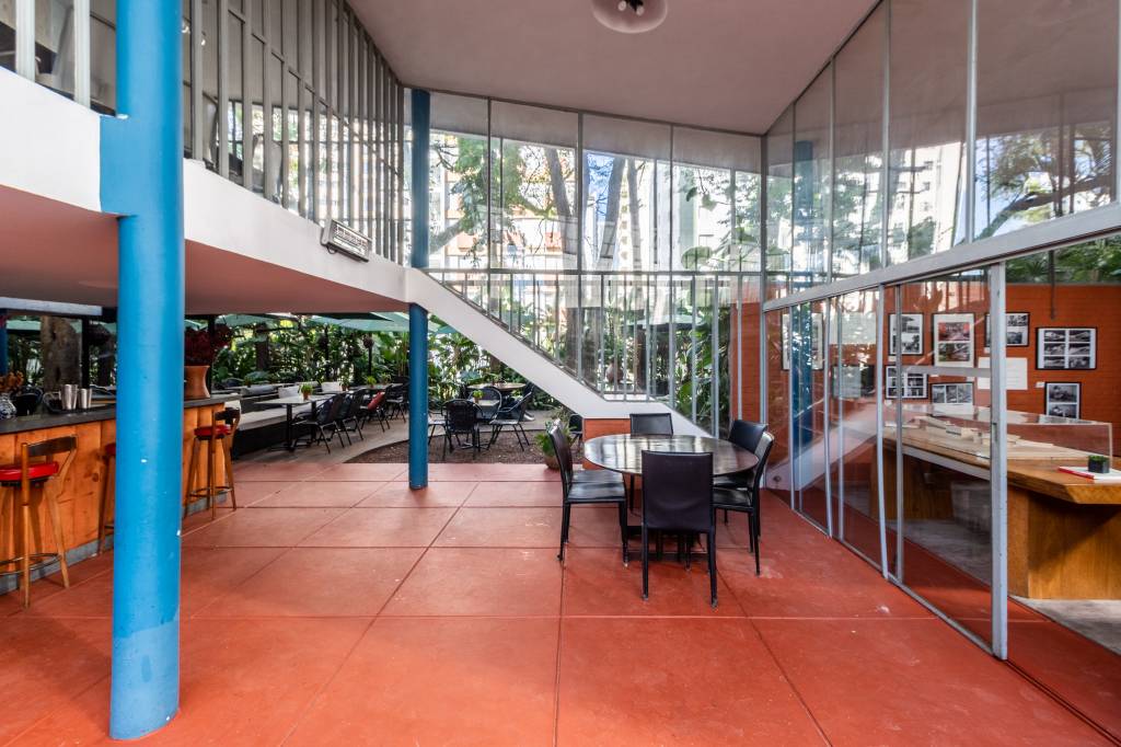 Segunda Residência de Vilanova Artigas – Campo Belo – 1949 – @o Chão laranja, segundo andar envidraçado e mesa com cadeiras pretas aparecem em destaque em sala aberta com jardim ao fundo.