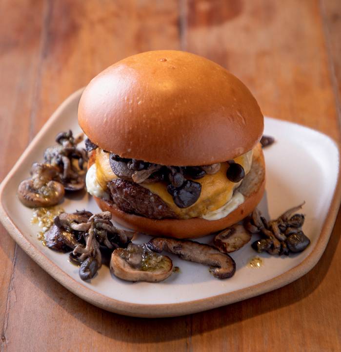 Hambúrguer com pão dourado, carne, queijo e cogumelos variados.