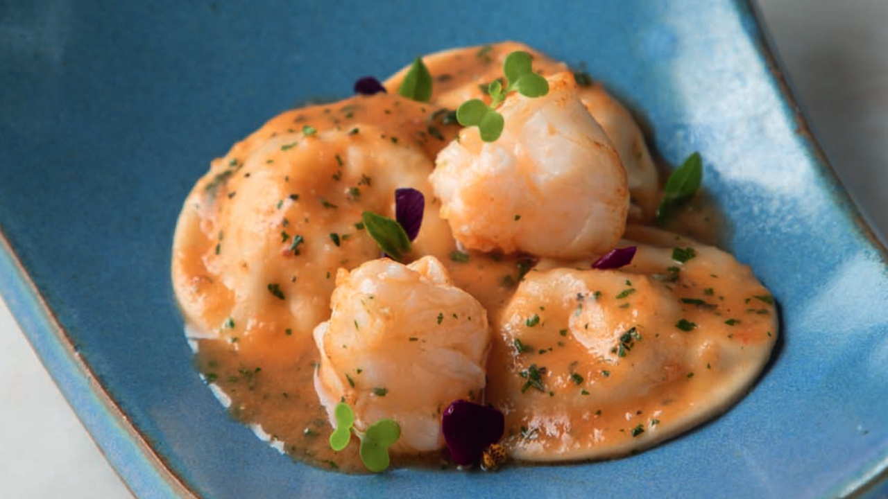 Prato de louça azul com ravioli e pedaços de lagosta.
