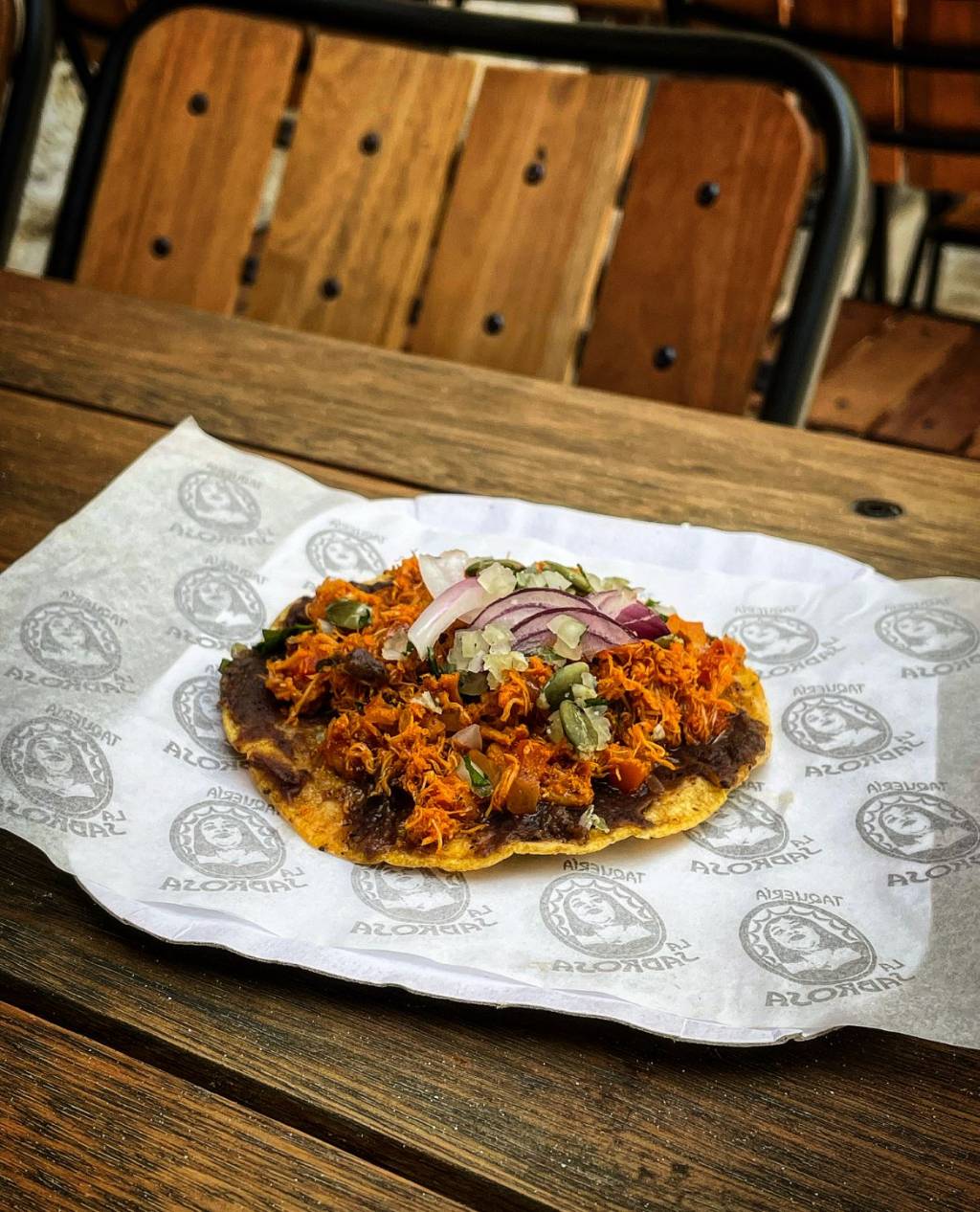 Taquería La Sabrosa Taco aberto sobre prato de papel em mesa de madeira.