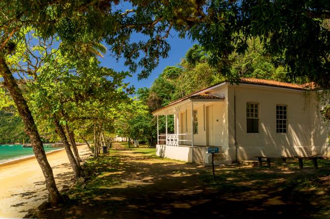 ubatuba ilha anchieta Imagem mostra pequena casa na costa de praia em local arborizado, com grama do lado da casa e areia próxima ao mar