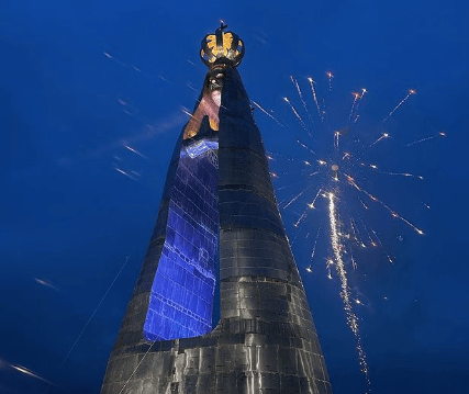 imagem mostra grande estátua de Nossa Senhora, com vão no meio e fogos de artifício no céu no momento da foto