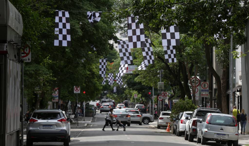 JOEL9818 Bandeiras quadriculadas espalhadas pela rua Oscar Freire, nos Jardins, e uma pessoa atravessando a rua. Carros aparecem estacionados dos dois lados.
