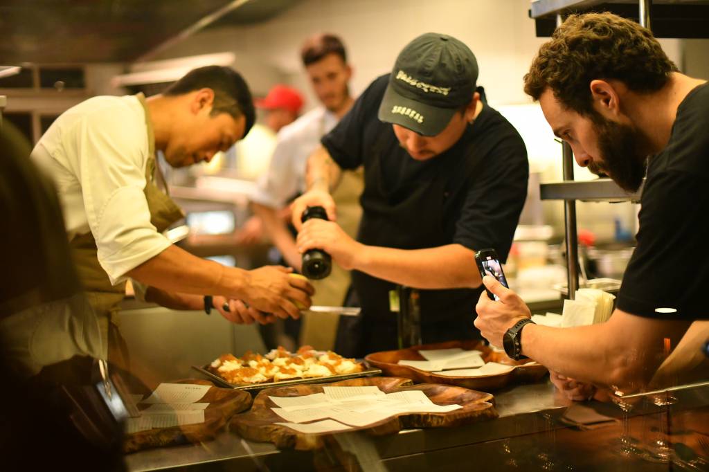 Jantar Circuito Comer & Beber Chef de preto atrás de balcão finalizando prato na boqueta