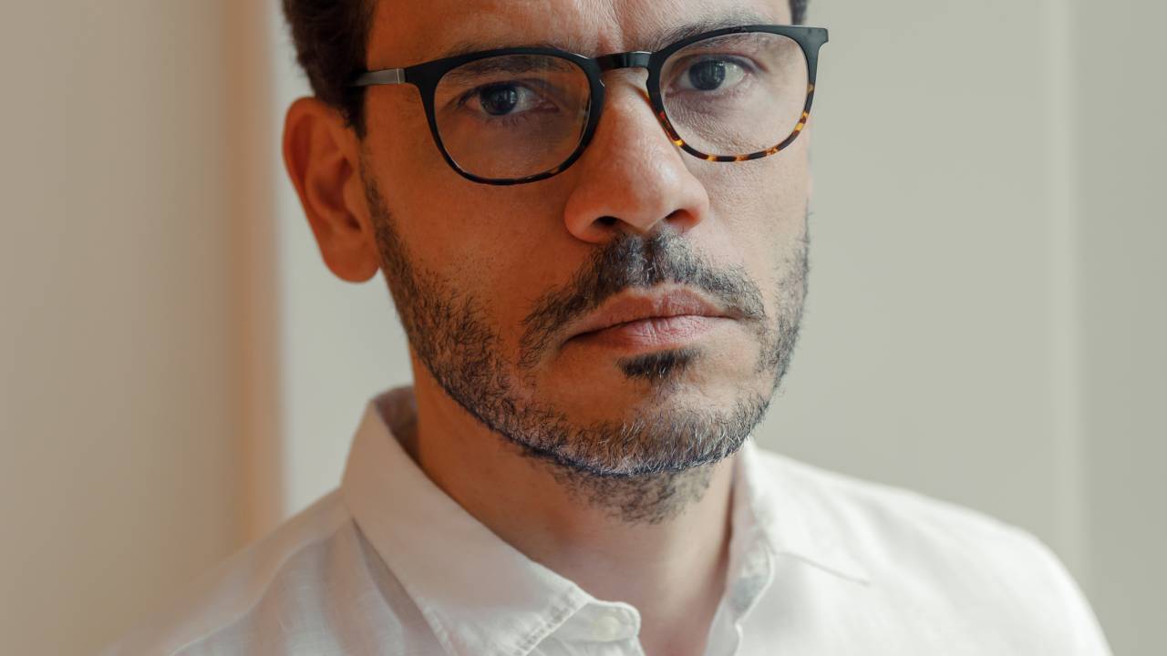 Homem de barba e óculos de grau vestindo camisa branca.