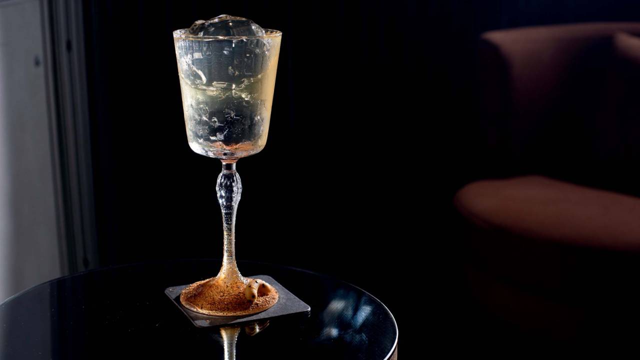 Uma taça de formato mais retangular com líquido translúcido e fundo preto.