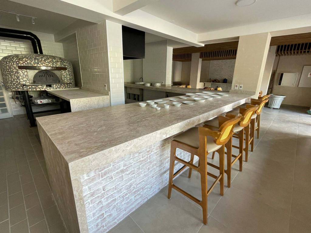 La Crosta Forneria – Água Fria Salão de pizzaria com bancada de mármore e banquetas de madeira em frente ao forno de pizza no canto esquerdo.