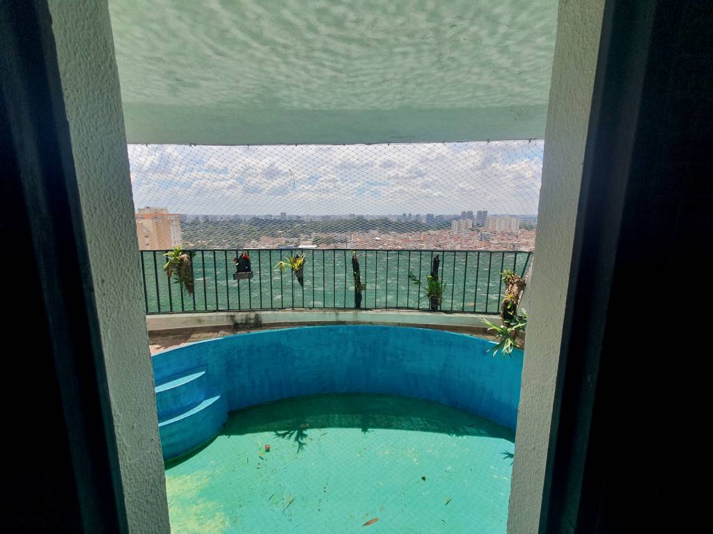 edifício penthouse Imagem mostra em primeiro plano piscina azul vazia e, ao fundo, vista para favela, com grade de sacada e plantas penduradas na sacada