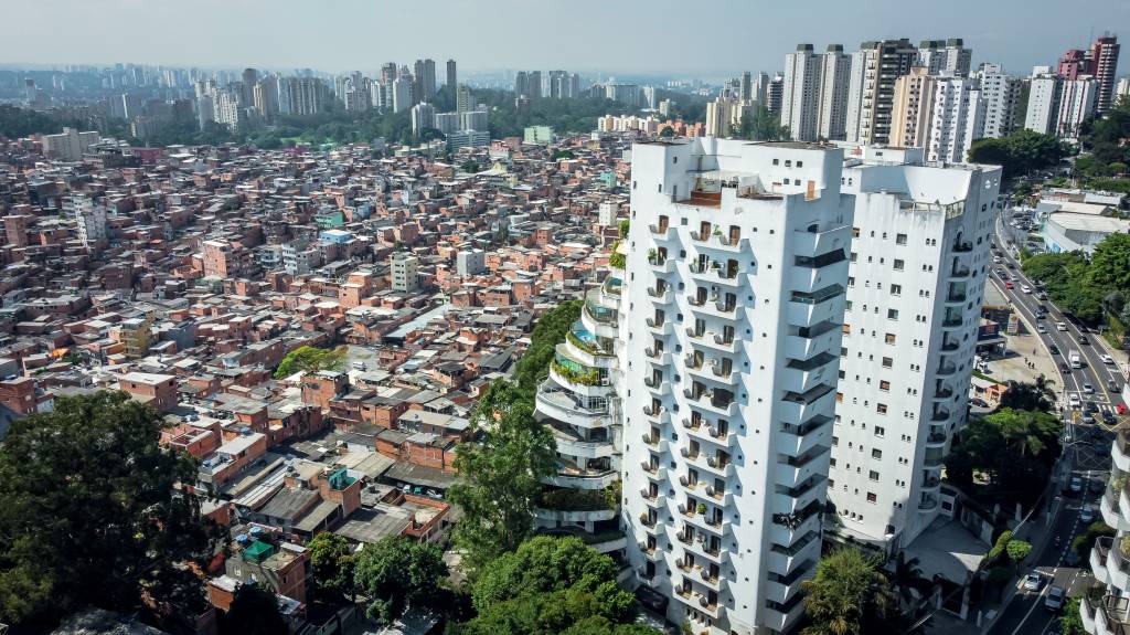 edifício penthouse Imagem mostra foto aérea de prédio com uma piscina por andar, com sacadas em espiral e, ao lado, favela, com pequenas casas, a maior parte com tijolos expostos. No canto direito, grande avenida movimentada
