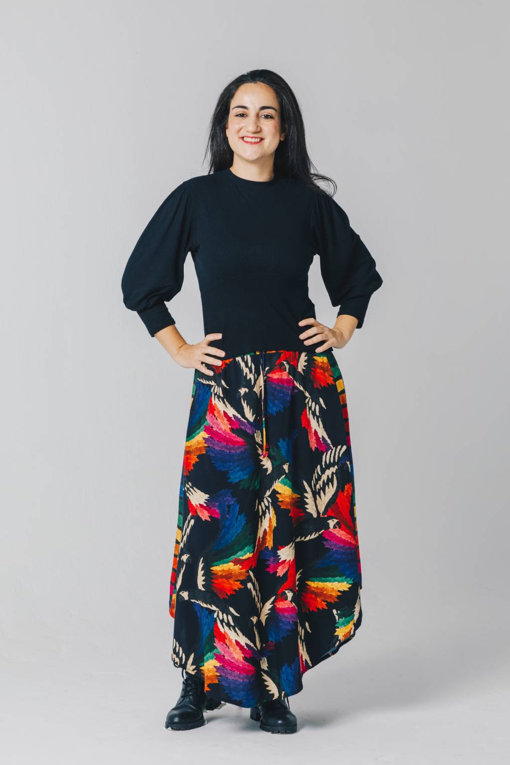 Daiane Barbieri-Crédito-Lana Pinho-Divulgação (1) Mulher branca de cabelos longos lisos posa com as mãos na cintura em fundo cinza claro. Veste blusa azul escuro e saia longa estampada