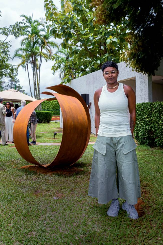 siwaju lima Imagem mostra Siwaju em pé em gramado, com grande obra de arte em formato circular ao fundo
