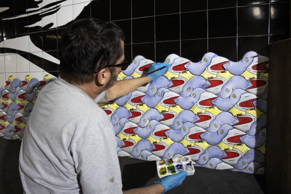 Antonio Peticov_Foto InfoArte (2) Foto exibe homem de costas restaurando mural de azulejos em corredor do metrô