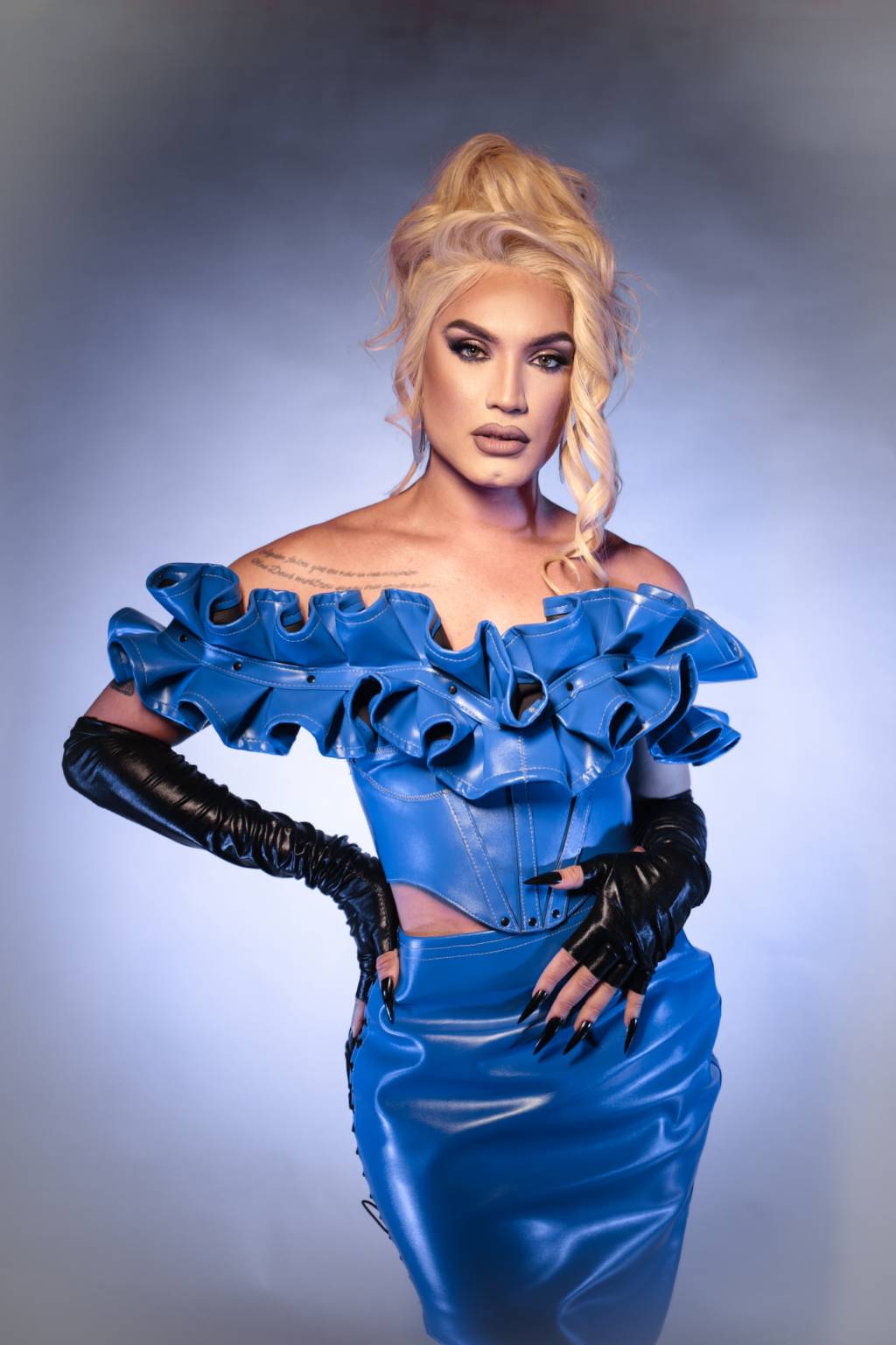 Aretuza Lovi-Crédito Maria Paula Freire-Divulgação (2) Drag queen loira veste traje azul com aparência de látex e babados na área do peito, além de luvas longas pretas.
