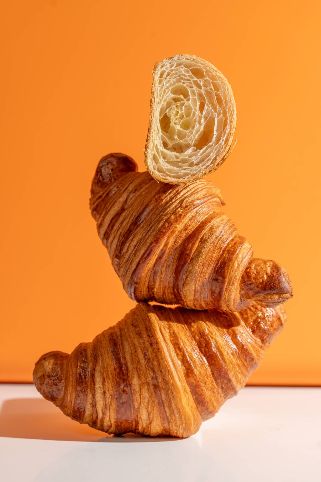 Kio Bakehouse Três croissants empilhados em frente a parede laranja com o último, em cima, cortado ao meio.