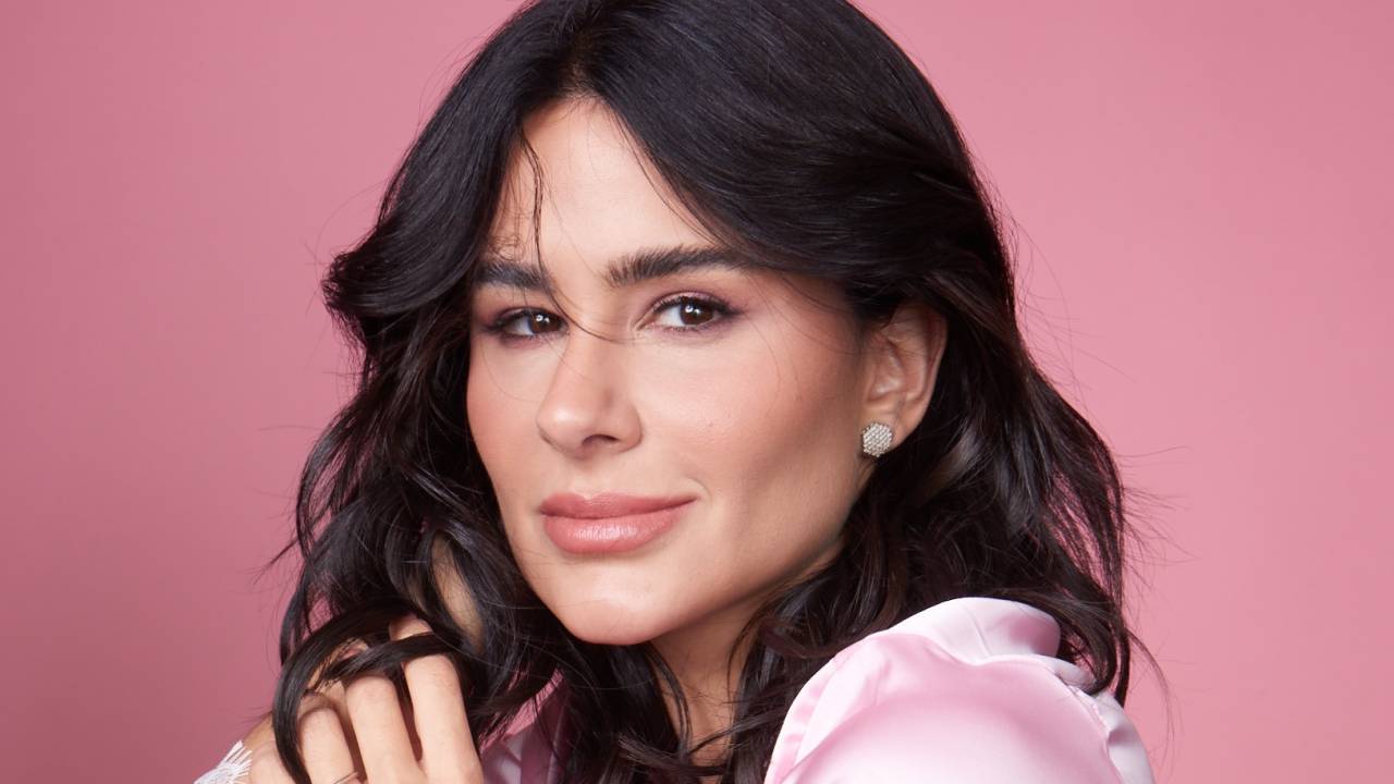 Moça branca de cabelos escuros curtos posa em fundo rosa e veste pijama rosado