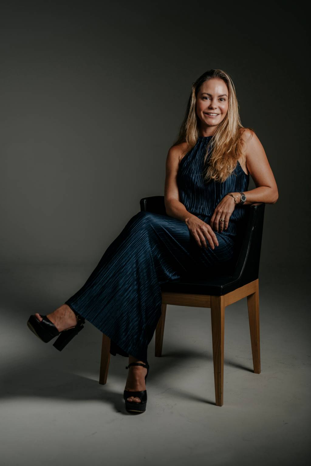 Paloma Horta-Crédito Torin Zanette-Divulgação (3) Mulher loira de vestido verde escuro sorri sentada em cadeira