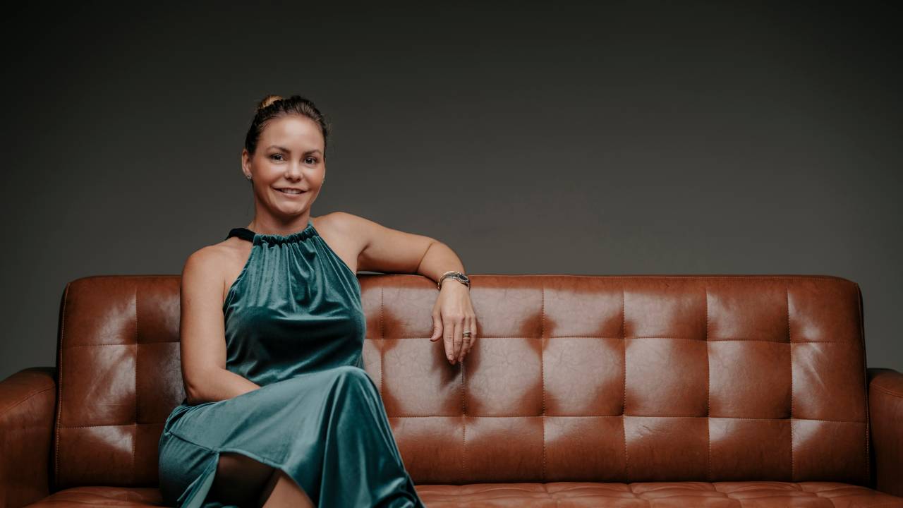 Mulher loira de vestido verde escuro sentada em sofá de couro