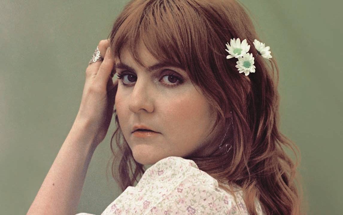 Mulher ruiva posa com mão na cabeça e flores no cabelo
