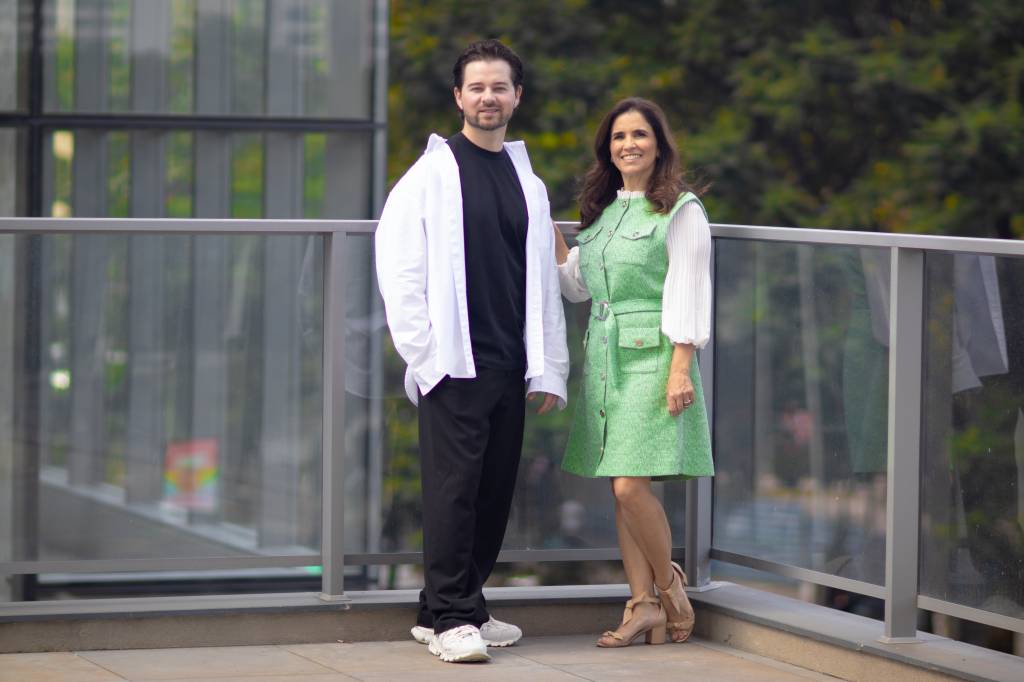 Rafael Bertolucci e Rosângela Barchetta-Crédito João Martinez-Divulgação (5) Moço e mulher posam em terraço, ela de vestido verde, ele de camisa branca e camiseta preta