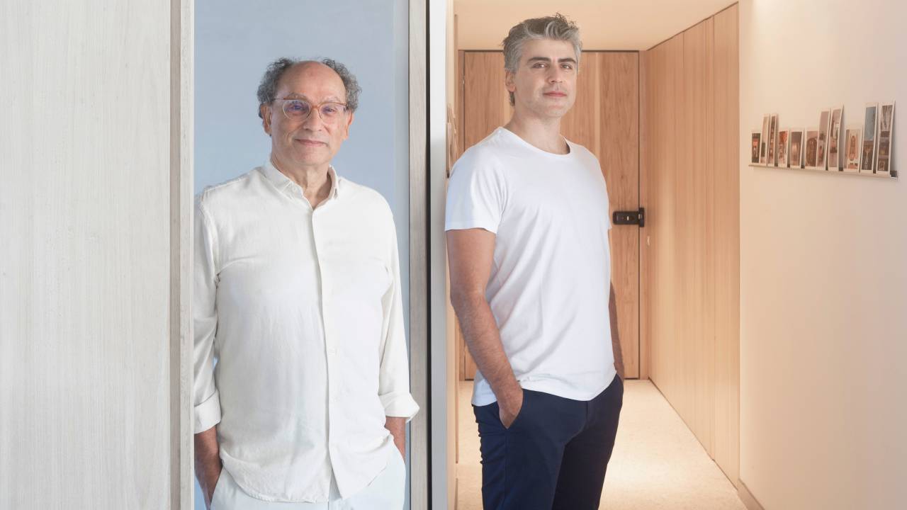 Dois homens grisalhos posam de pé vestindo branco