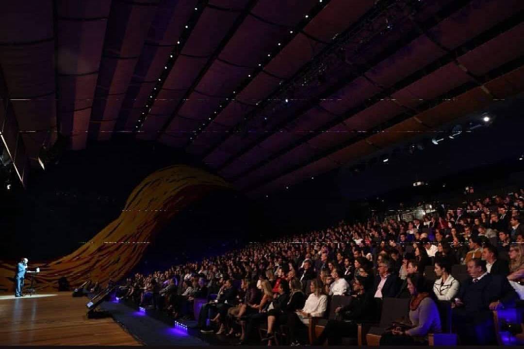 Foto de plateia lotada à direita e palco á esquerda.