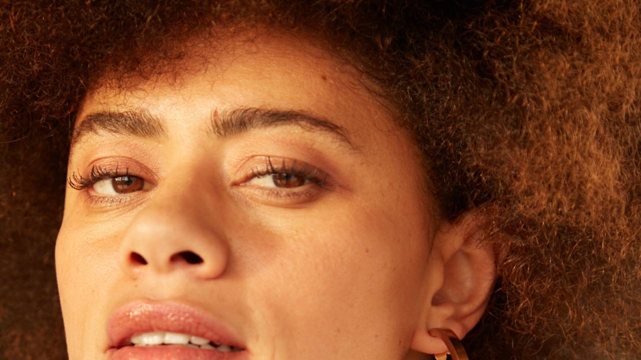 Mulher negra posa com brincos dourados e cabelos crespos volumosos