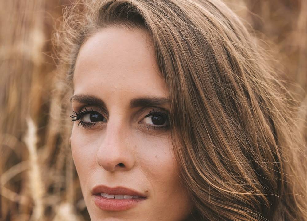 Mulher branca de cabelos longos encara a câmera e veste peça azul
