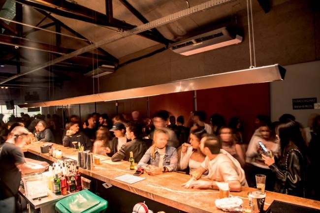 Caracol Foto de bar tirada de trás do balcão com pessoas em pé apoiados no balcão e ocupando o espaço ao fundo.