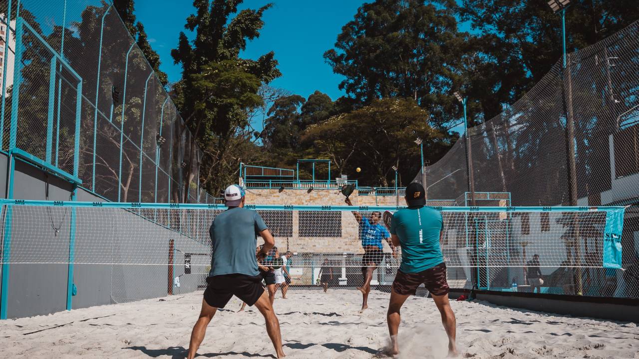Quadra de beach tennis com jogadores vestidos de shorts preto e camiseta azul