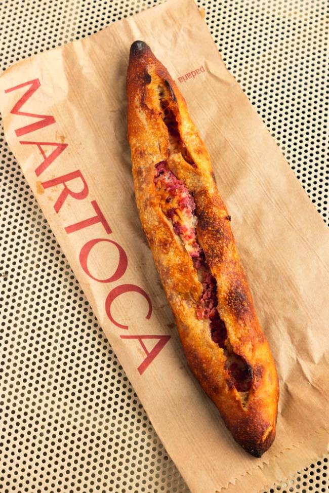 Baguete com linguiça em cima de papel com logo da padaria