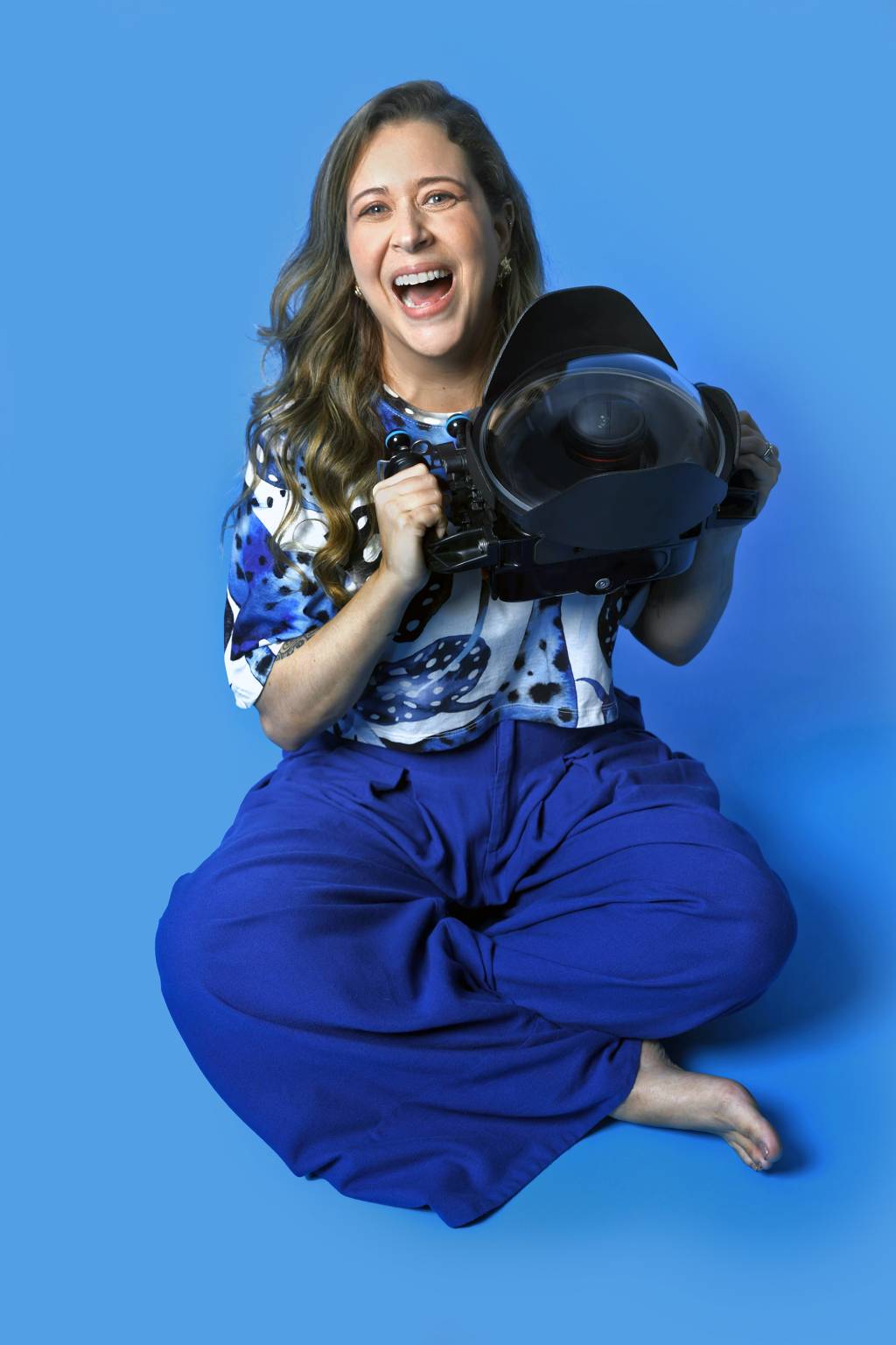 Fabi Fregonesi Crédito Luciana Aith-Divulgação (3) Mulher de conjunto azul posa sentada segurando equipamento de fotografia