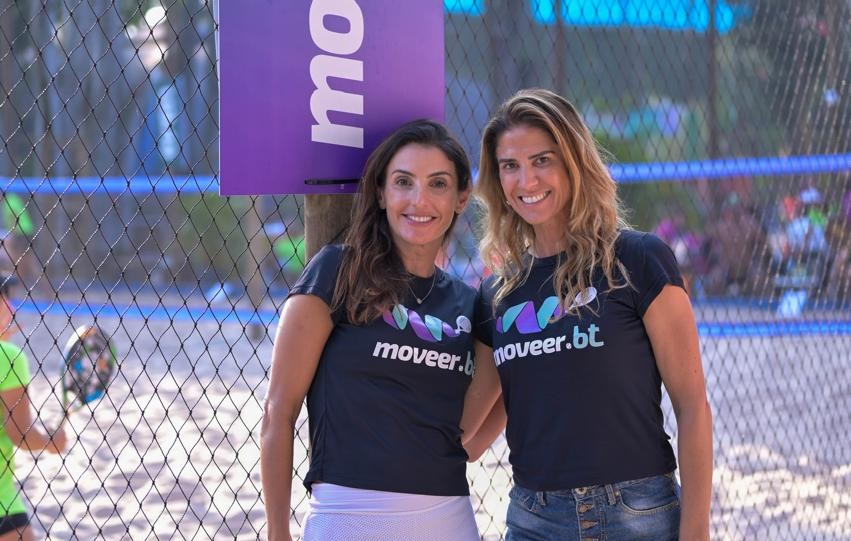 Duas mulheres de roupas esportivas sorriem em quadra de beach tennis