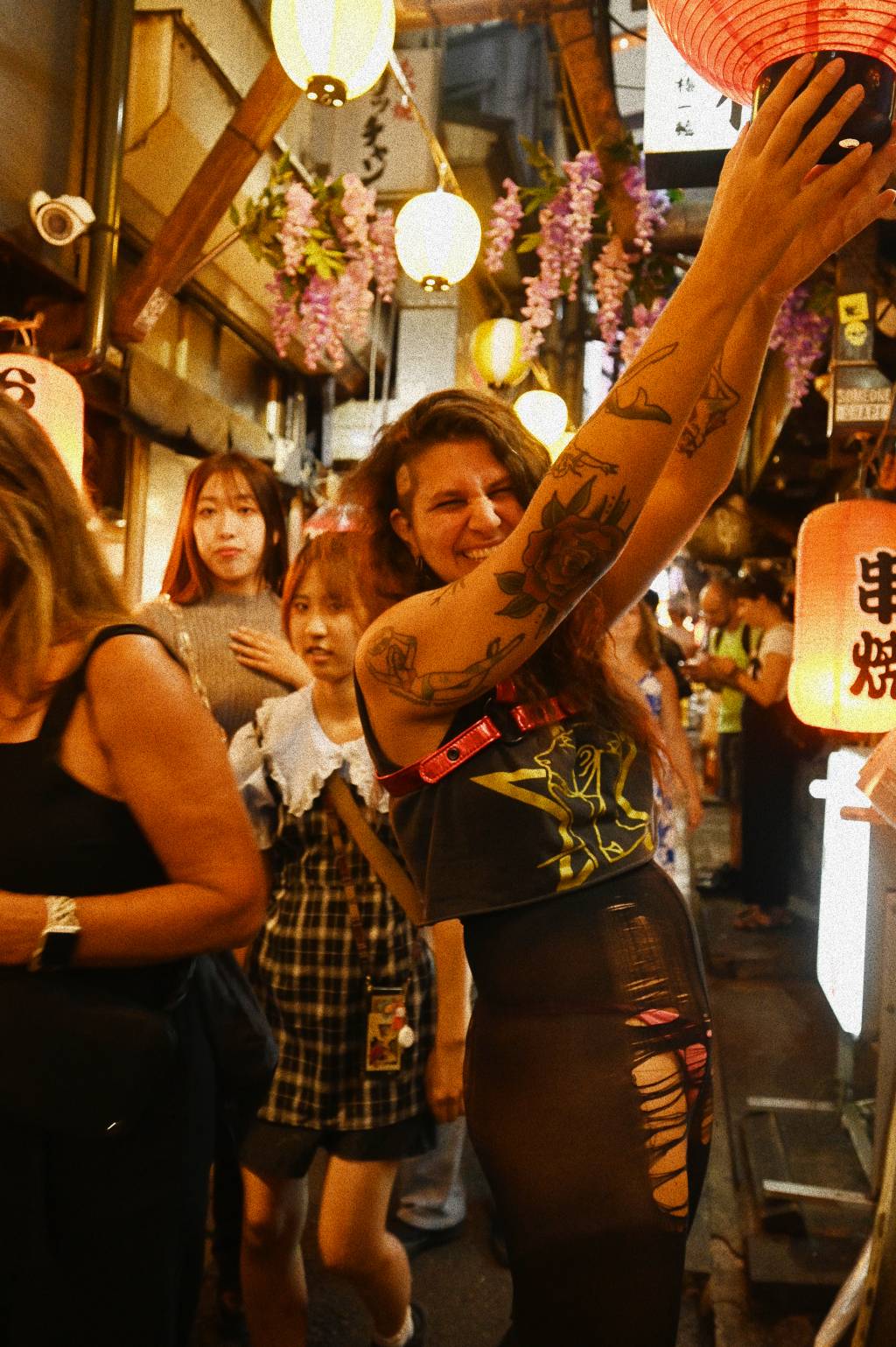 Suzana Haddad Crédito Michiya Takahashi-Divulgação (8) Mulher branca de cabelos encaracolados longos posa rindo e segurando lâmpada japonesa em corredor estreito de turistas