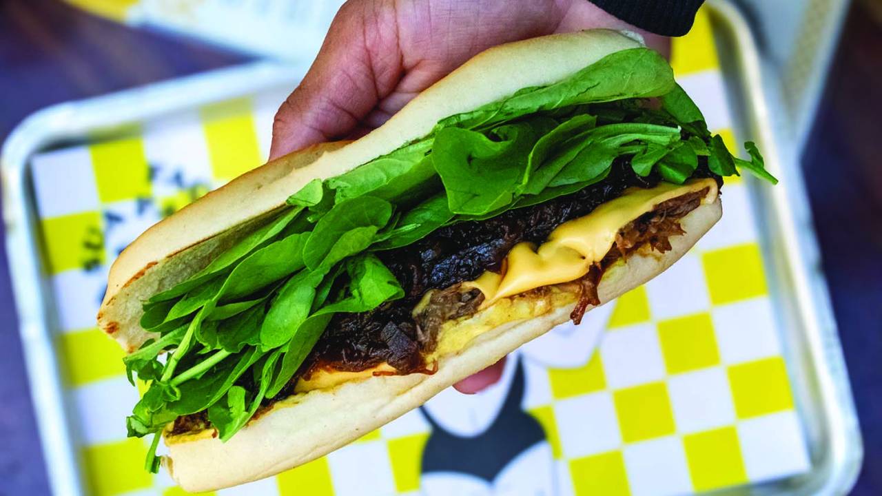Mão segurando sanduíche de carne de panela e queijo