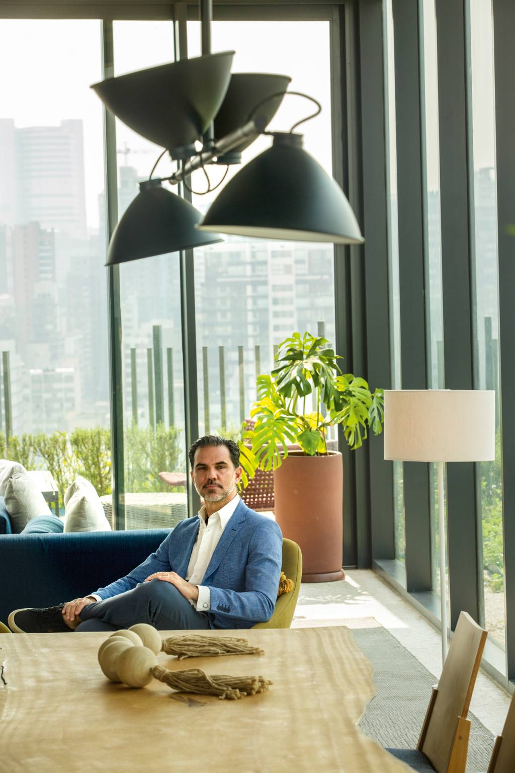0040 Viola Edificio Ayra.jpg Homem grisalho de terno azul sentado em sofá atrás de mesa em sala com vidraças