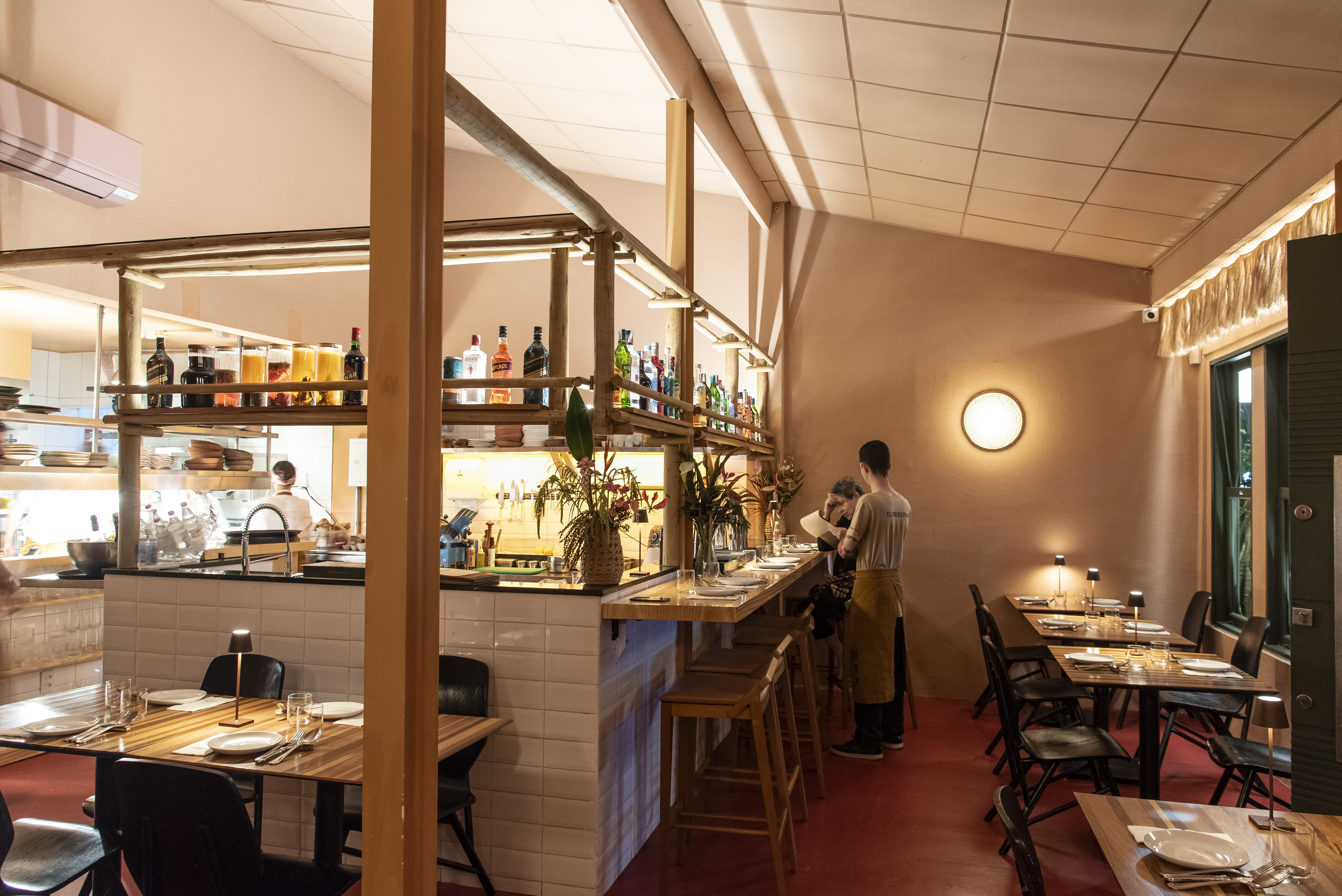 Sal&atilde;o de restaurante com fileira de mesas &agrave; direita e bar aberto &Agrave; esquerda.