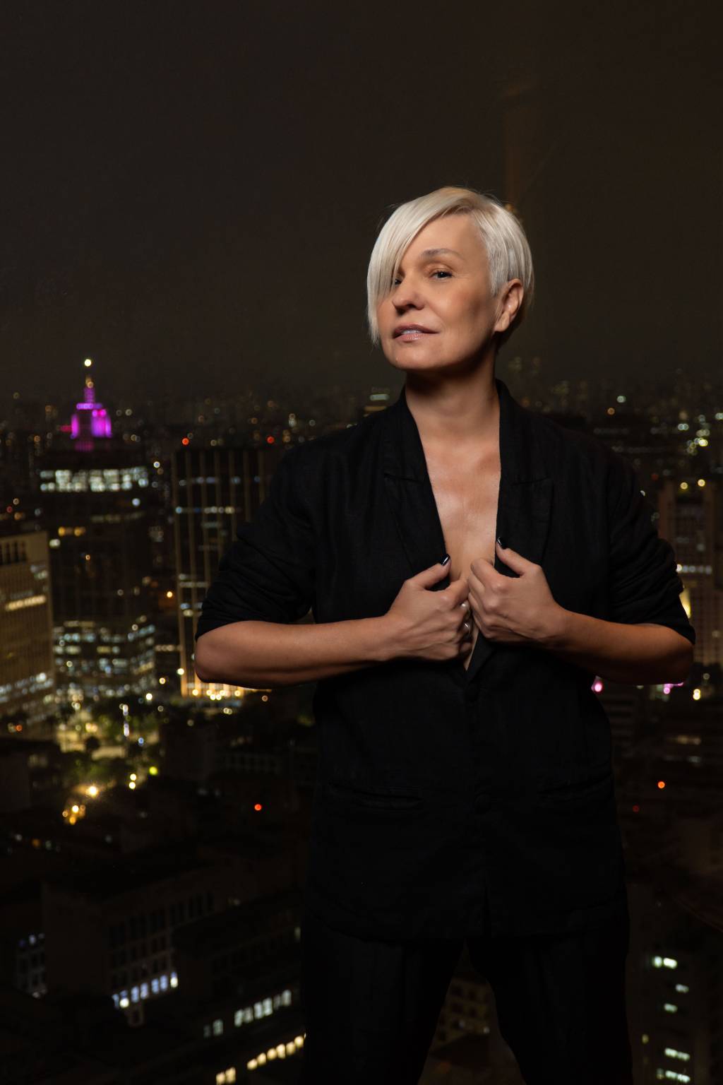ERIKA PALOMINO_8334_limpo Moça loira de cabelo curto posa com blazer preto e cidade do alto aparece ao fundo